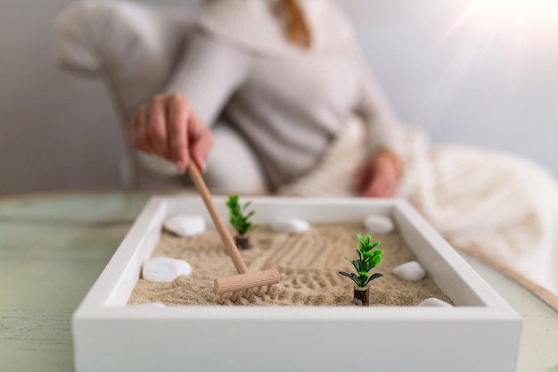 Mano di bella giovane donna che usa il suo giardino Zen a casa. Bella giovane donna sorridente che si rilassa con il suo giardino Zen e si gode la giornata