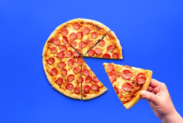 Mano di donna che prende una fetta di pizza sopra vista Deliziosa pizza ai peperoni isolata su sfondo blu