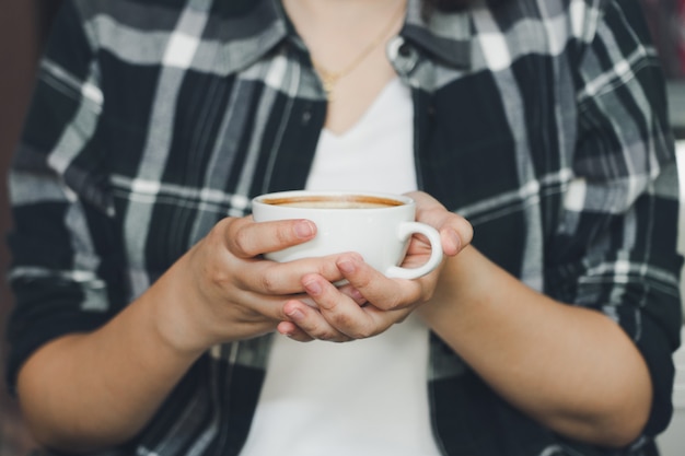 Mano di donna che tiene una tazza di caffè bianco. Il caffè è un latte.