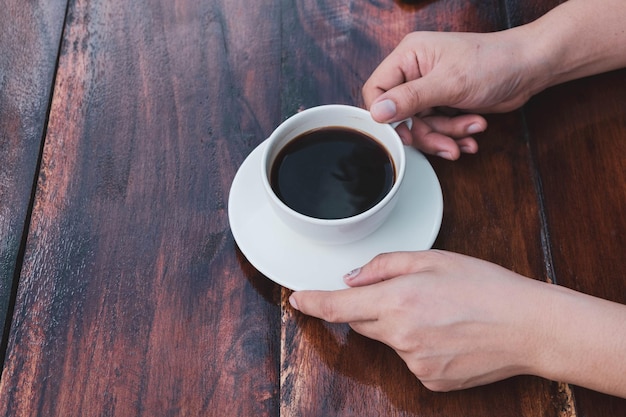 Mano di donna che tiene una tazza di caffè su un tavolo di legno