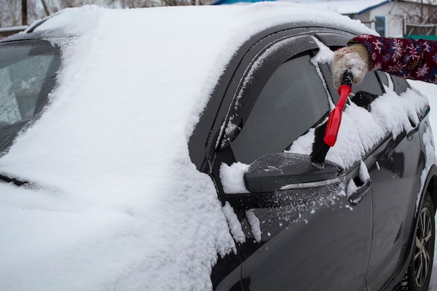 Mano di donna che usa la spazzola e rimuove neve e ghiaccio dall'auto e dal parabrezza concetto di trasporto ...