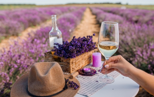 Mano di donna con bicchiere di vino bianco su uno sfondo di campi di lavanda in Provenza Francia Linee di cespugli di fiori viola