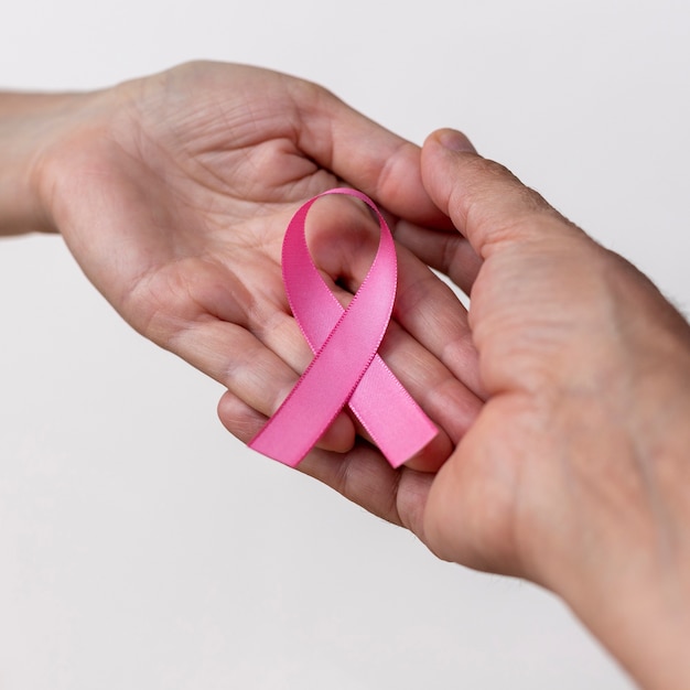 Mano di donna con nastro rosa e mano di uomo a sostegno della campagna di sensibilizzazione sul cancro al seno di ottobre rosa