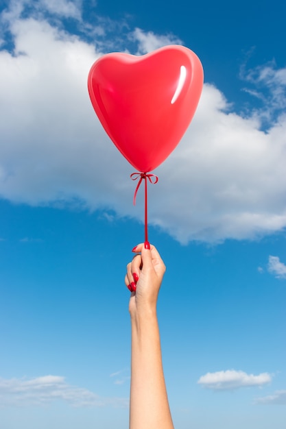 Mano di donna con palloncino a forma di cuore sullo sfondo del cielo
