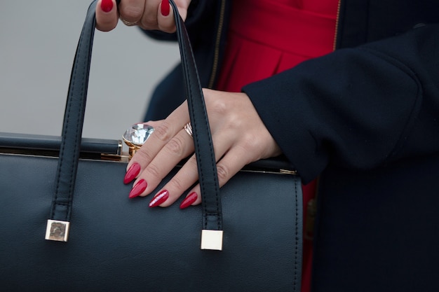 Mano di donna con una bella manicure rossa che tiene una borsa in pelle nera
