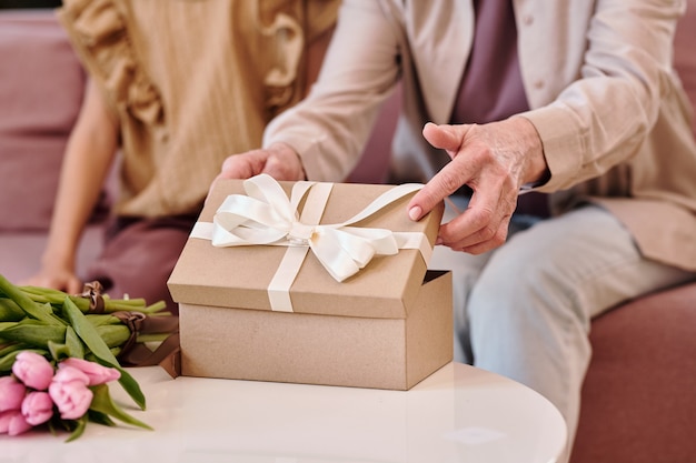 Mano di donna matura che apre scatola regalo con regalo di compleanno