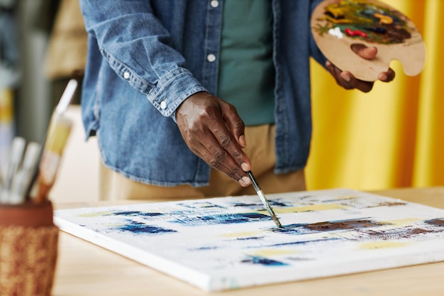 Mano di giovane artista maschio afroamericano con tavolozza di colori pittura con colori acrilici su tela