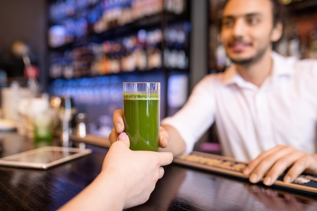 Mano di giovane donna che prende un bicchiere di stipendio fresco o frullato di broccoli passato da cameriere o barman in un ristorante di classe