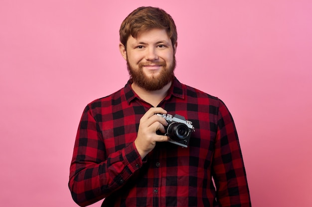 Mano di giovane uomo ispanico tenendo la fotocamera vintage isolato su sfondo rosa