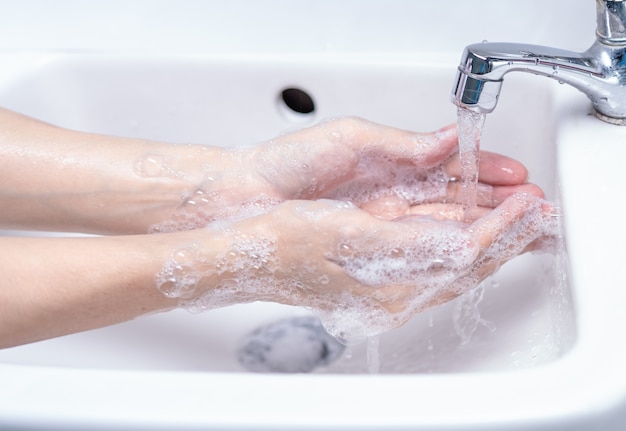 Mano di lavaggio della donna con schiuma di sapone e acqua di rubinetto