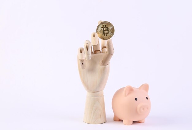 Mano di legno che tiene bitcoin e salvadanaio su sfondo bianco