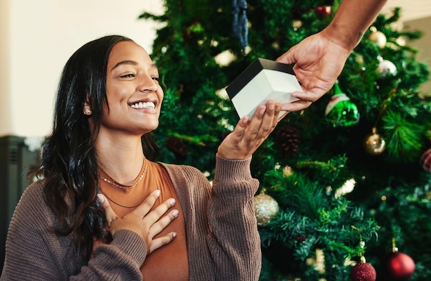 Mano di Natale con regalo e donna con sorriso coppia e scambio di regali sorpresa e felice di celebrare l'amore e la cura dell'albero di Natale con la celebrazione della scatola e la tradizione festiva