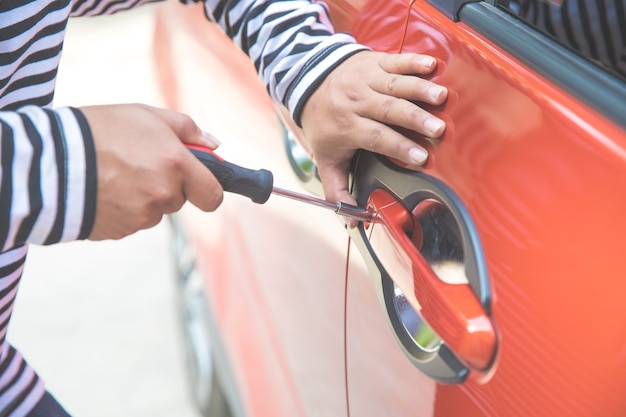 mano di primo piano del ladro tenta di rompere in auto con un cacciavite