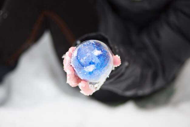 Mano di un bambino che tiene una palla blu. Palla blu nel palmo della mano su uno sfondo di neve.