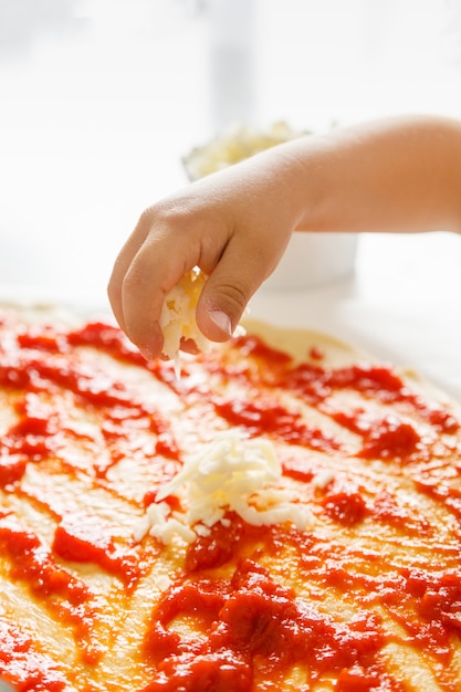 Mano di un bambino piccolo che getta formaggio grattugiato su una pizza