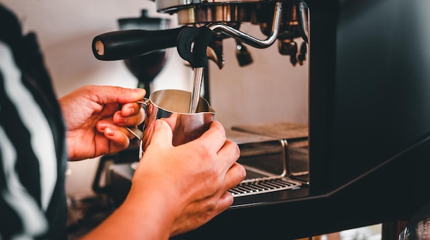 Mano di un barista nella caffetteria che prepara e utilizza una macchina da caffè per cuocere a vapore il latte per un caffè