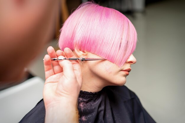 Mano di un parrucchiere che taglia il rosa corto con i capelli a forbice in un salone di parrucchiere, primo piano, vista laterale.