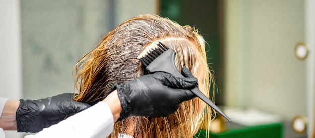 Mano di un parrucchiere in guanti neri che applicano tintura ai capelli femminili in un salone di bellezza beauty