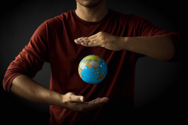 Mano di un uomo che protegge un globo che galleggia tra la sua mano su sfondo nero. Concetto di giornata per la terra