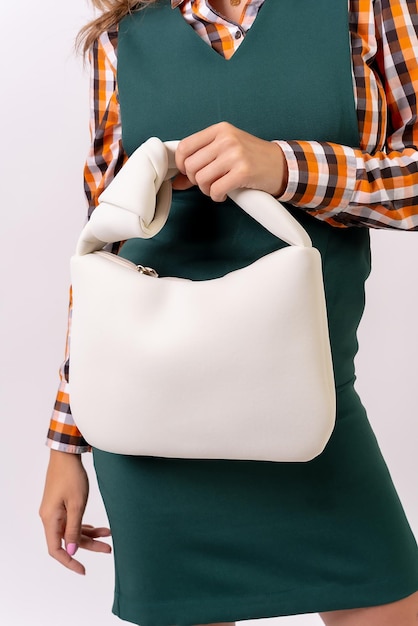 Mano di una donna d'affari con una borsetta crema su uno studio di moda sfondo bianco