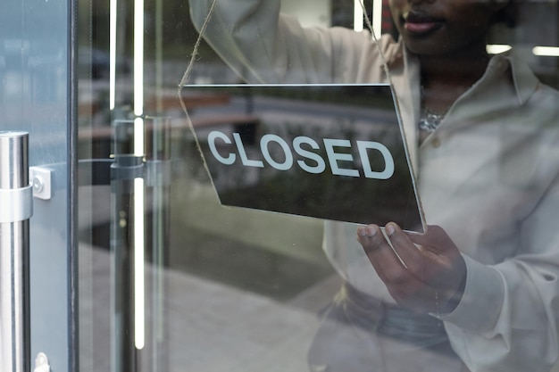 Mano di una giovane donna africana che mette un avviso sulla porta di vetro della boutique