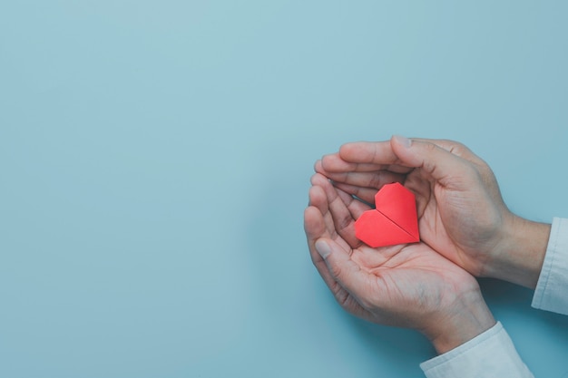 Mano di uomo d'affari che tiene carta cuore rosso con segnale d'onda del cuore su sfondo blu. È il concetto di condizione del controllo sanitario.