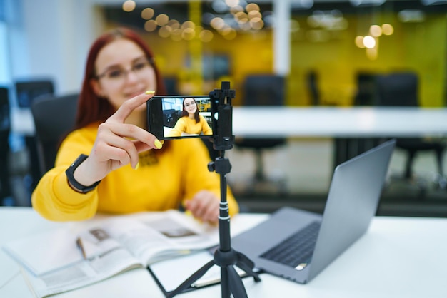 Mano donna che tiene la fotocamera per la registrazione di video Studente adolescente in un maglione giallo con laptop