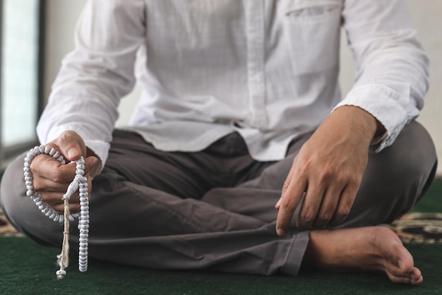 Mano e gambe incrociate dell'uomo musulmano che prega nella moschea tenendo perline di preghiera