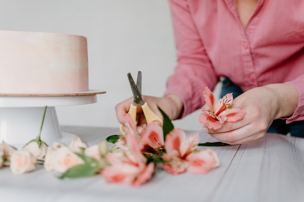 Mano femminile che decora la torta di compleanno rosa di nozze del fiore sul supporto.