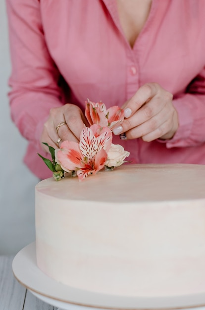 Mano femminile che decora la torta di compleanno rosa di nozze del fiore sul supporto.