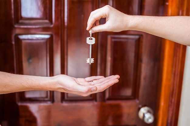 Mano femminile che fornisce una chiave per l'uomo della casa su fondo della porta di legno. Possedere il concetto immobiliare