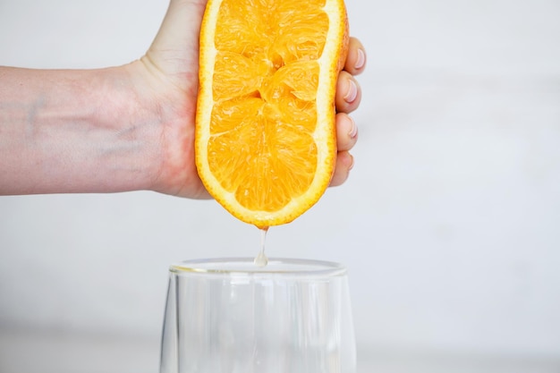 Mano femminile che schiaccia metà del succo d'arancia fresco degli agrumi sotto la bevanda naturale della colazione sana di vetro trasparente