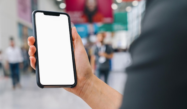 Mano femminile che tiene cellulare nero con schermo bianco in una fiera, copyspace per il tuo testo individuale.