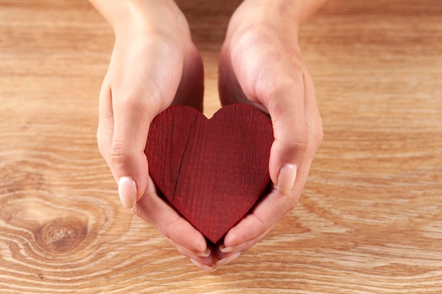 mano femminile che tiene il concetto di cura di amore del cuore di legno rosso