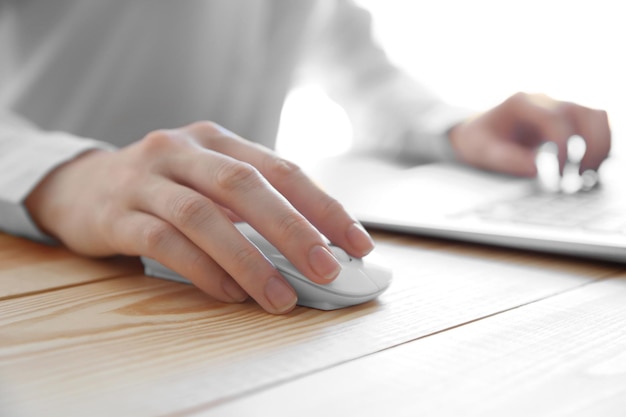 Mano femminile che tiene il mouse del computer sulla tavola di legno