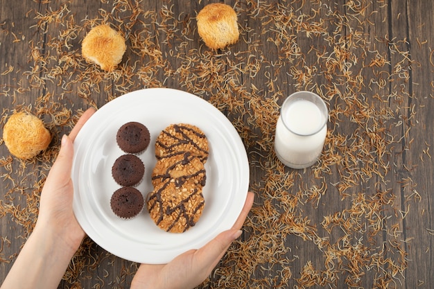 Mano femminile che tiene il piatto di biscotti dolci su una superficie di legno