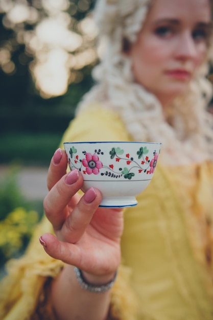 Mano femminile che tiene la lussuosa tazza di caffè medievale vicino al fuoco selettivo