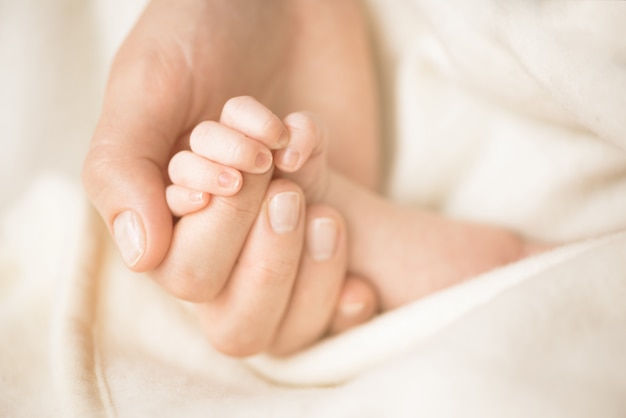 Mano femminile che tiene la mano del suo bambino appena nato. Mamma con il suo bambino Maternità, famiglia, concetto di nascita.