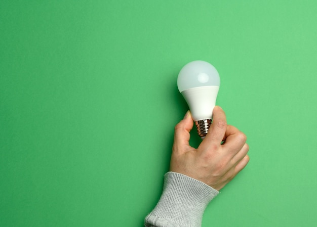 Mano femminile che tiene lampada in vetro bianco, energia verde