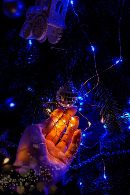 Mano femminile che tiene le decorazioni dell'albero di Natale di notte. Luce blu brillante della ghirlanda. Momenti magici di Capodanno. Fiaba. Magia del Natale