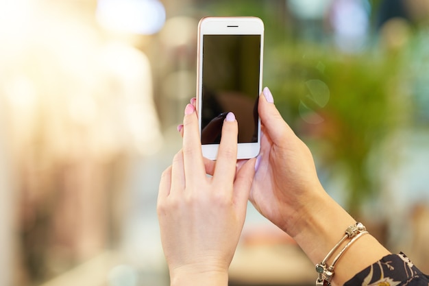 mano femminile che tiene smartphone nel negozio di vestiti