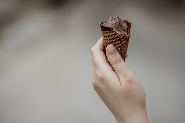 Mano femminile che tiene un cono gelato al cioccolato. Dolce estivo fresco e freddo.