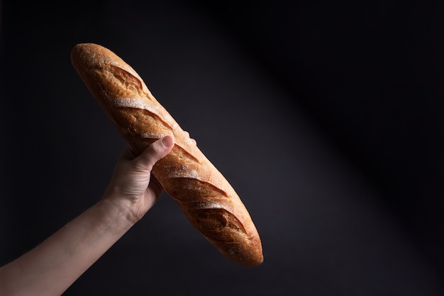 Mano femminile che tiene una baguette francese croccante su un nero