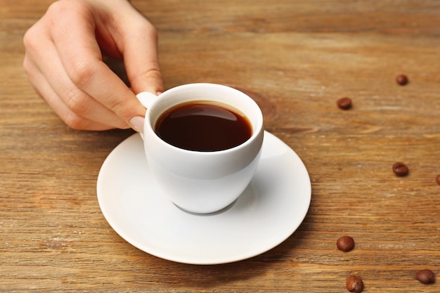 Mano femminile che tiene una tazza di caffè con grani su sfondo di legno