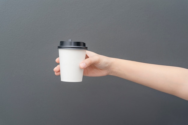 Mano femminile che tiene una tazza di carta del caffè su gray