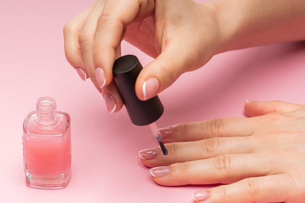 Mano femminile con bella manicure francese che applica smalto rosa