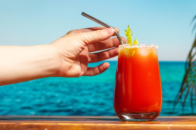 Mano femminile con cocktail Bloody Mary sulla spiaggia tropicale