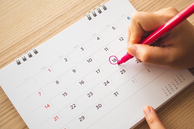 Mano femminile con segno di penna sulla data del calendario