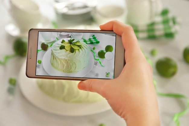 Mano femminile con smartphone che fa foto di un primo piano cremoso di torta al lime