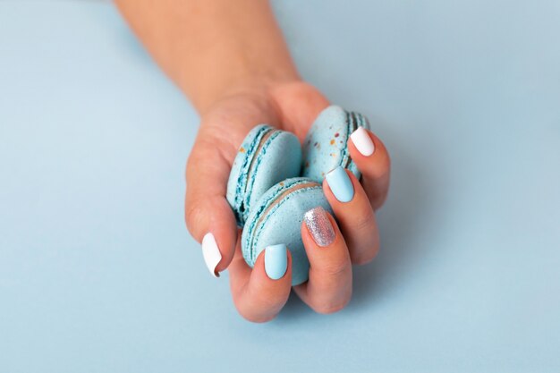 Mano femminile con unghie manicure blu che tengono amaretti dolci